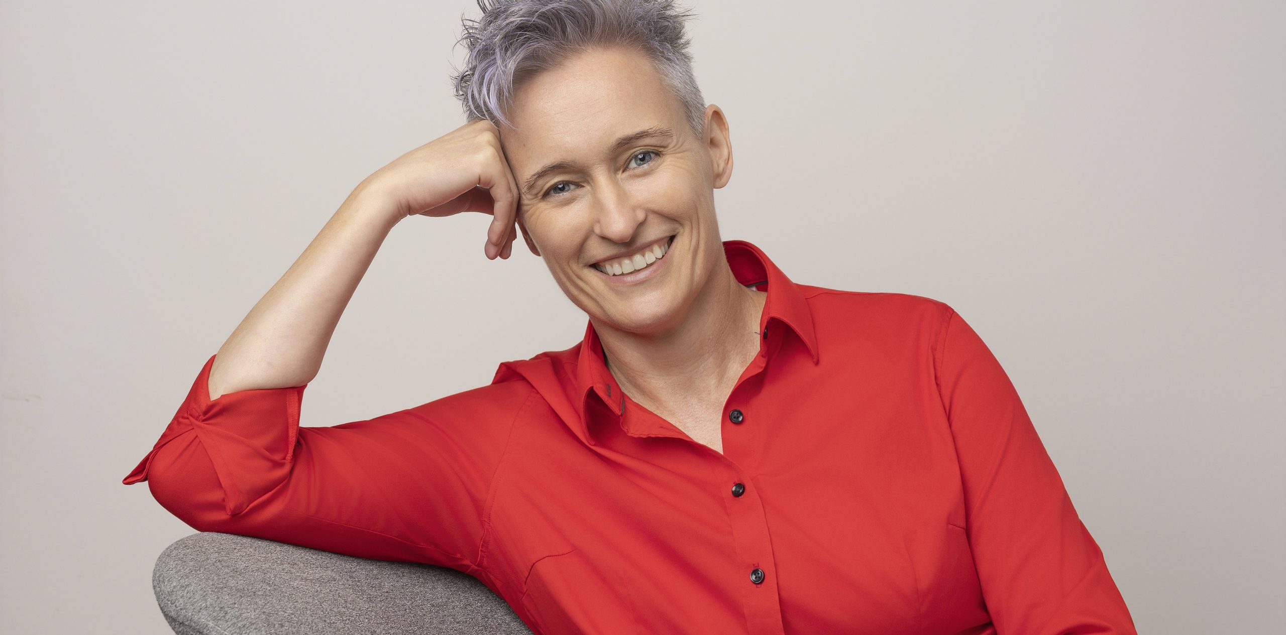 Bewerbungsbild Frau mit grauen Haaren und roter Bluse auf grauem Stuhl